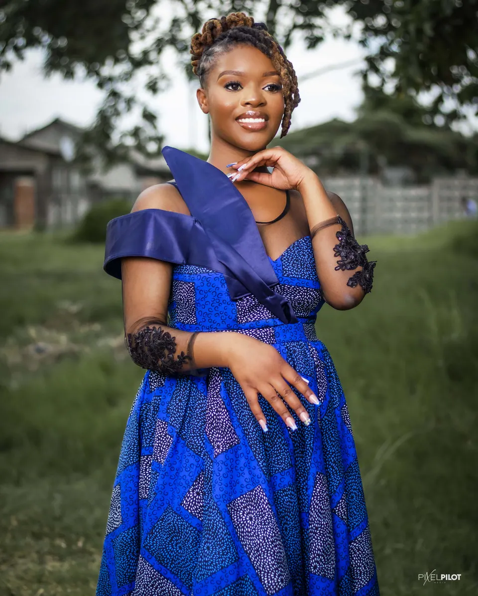 Woman in a blue African-print dress with a satin shoulder piece in a garden