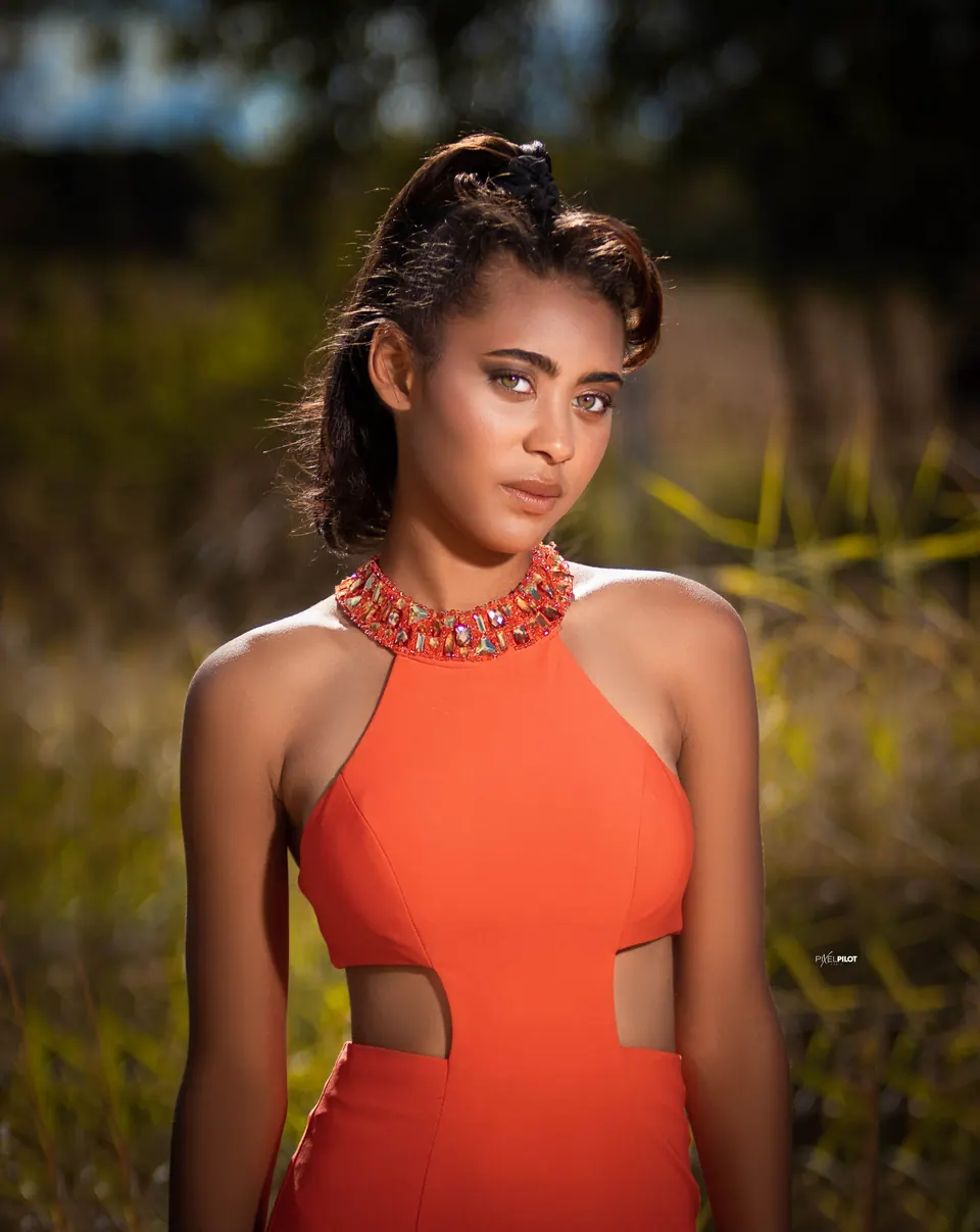 Close portrait of a woman in an orange halter gown in a golden field